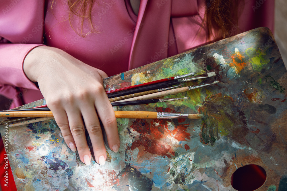 woman in a pink jacket stands with paints, brushes and palette on the street