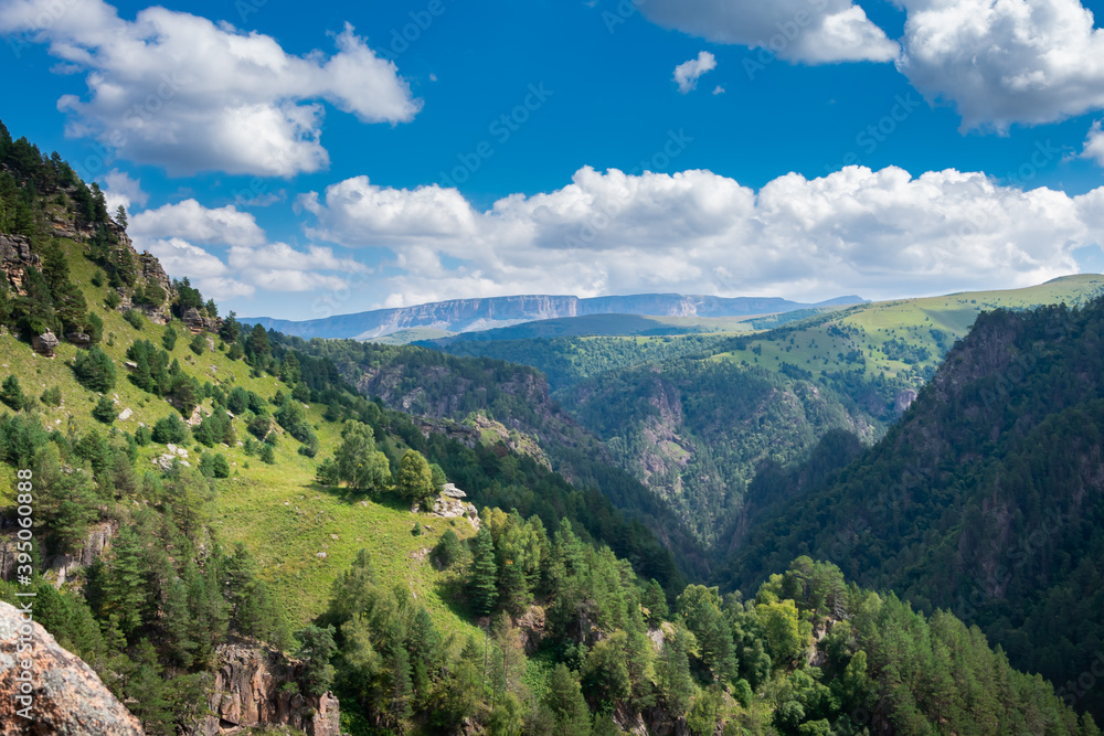 Obraz premium Beautiful landscape of mountainous woodlands and white clouds in the sun. Mountain ranges, top view, close-up. Mountain peak.