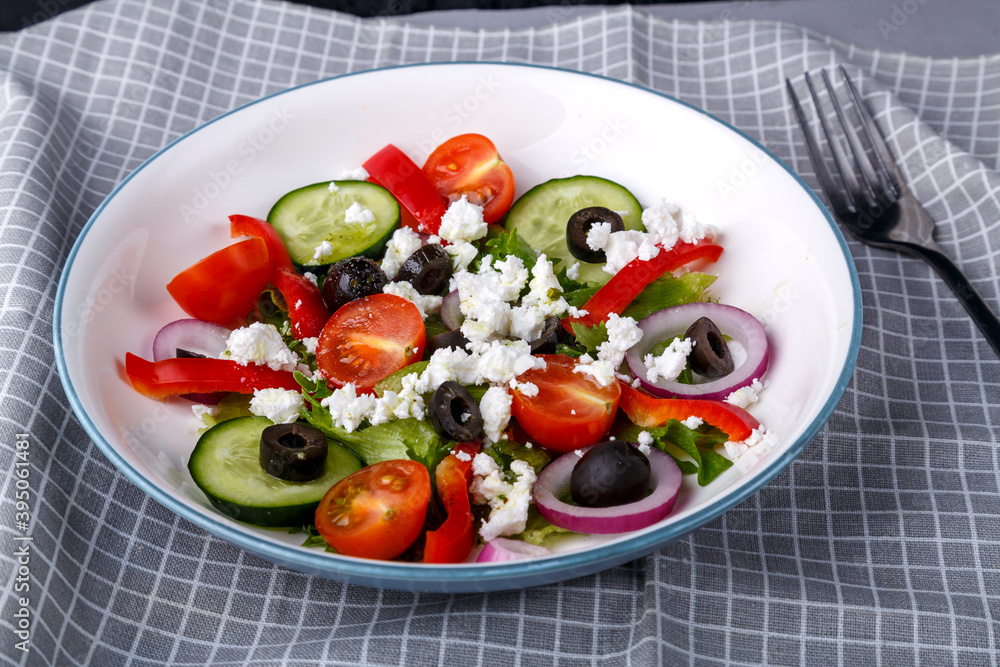 Light plate of Greek salad on a checkered napkin with a fork.
