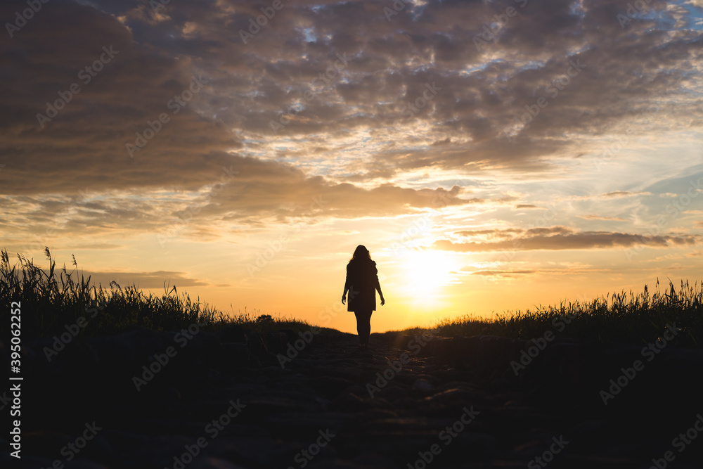 sunset on the beach with rocks and sea and silhouette of a woman