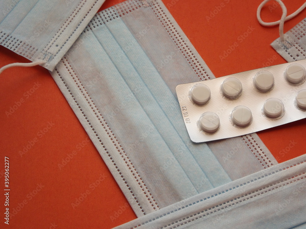 Blue protective medical masks and white tablets on an orange background. High quality photo Blue protective medical masks and white tablets on an orange background. High quality photo
