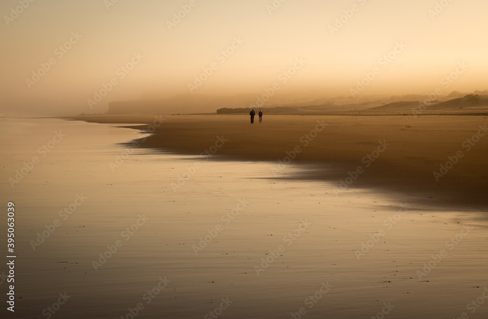 A couple walks in the mist of a beautiful sunrise on the beach of bordeira (Portugal)