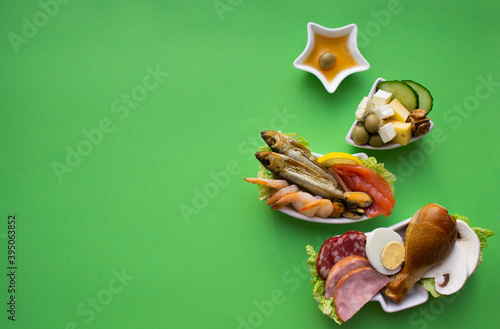 Fototapeta Naklejka Na Ścianę i Meble -  Plate in the form of a Christmas tree with protein food - meat, fish, cheeses, nuts, etc. Green background. The concept of keto diet treats for the holiday. Copy space