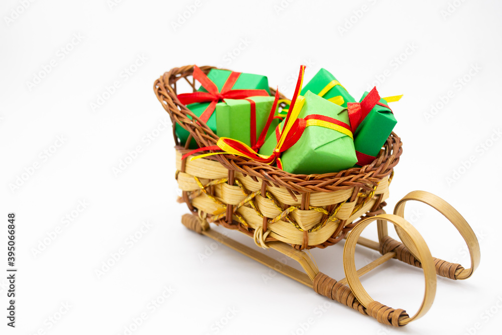 Old-fashioned wicker Santa sleigh with Christmas gifts wrapped in green paper with red ribbon