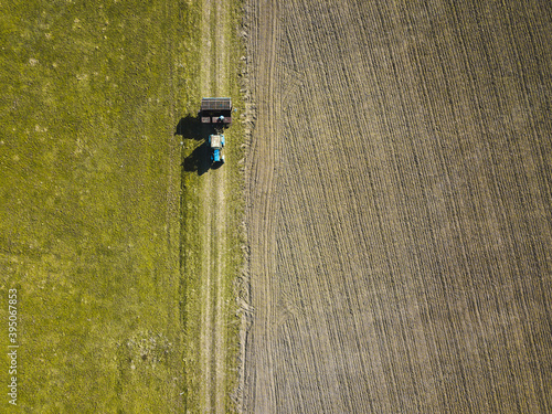 drone shot with grass in the country side and a tractor and plowed field