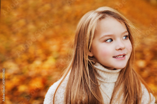 Portrait of blue-eyed little girl in wight autumn sweater in autumn park