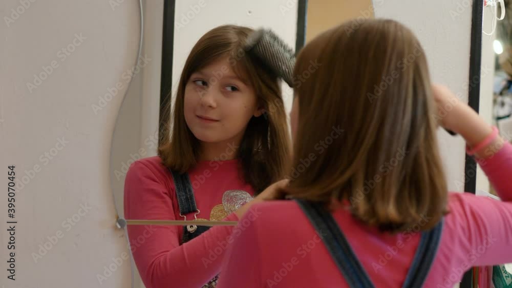 a girl is combing her hair in front of the mirror at home