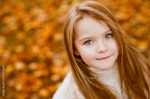 Portrait of blue-eyed little girl in wight autumn sweater in autumn park