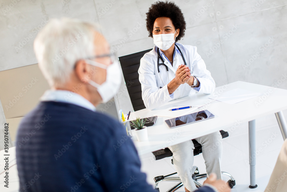 Naklejka premium Senior couple with protective facial masks receive news from black female doctor