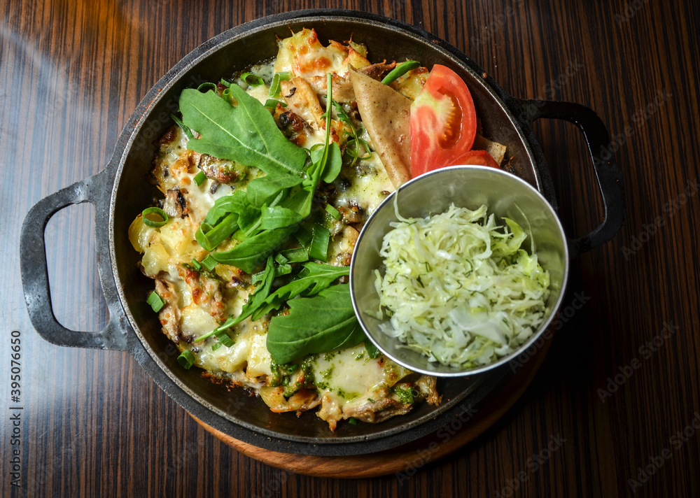 Appetizing pan with fried potatoes with meat and cheese, supplemented with greens, salad and tomato Appetizing pan with fried potatoes with meat and cheese, supplemented with greens, salad and tomato