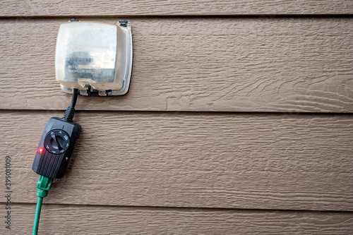 Outdoor timer and GCFI outlet with cover.  Brown siding on residential building photo