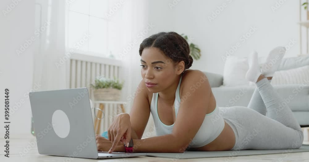 Young african american lady browsing on laptop, searching fitness video tutorial before workout at home Young african american lady browsing on laptop, searching fitness video tutorial before workout at home