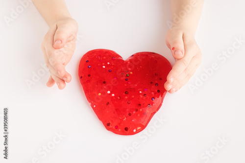 Red slime in heart shape in kid hands. Kid hands playing slime toy on white background. Making slime. Love and valentines day concept