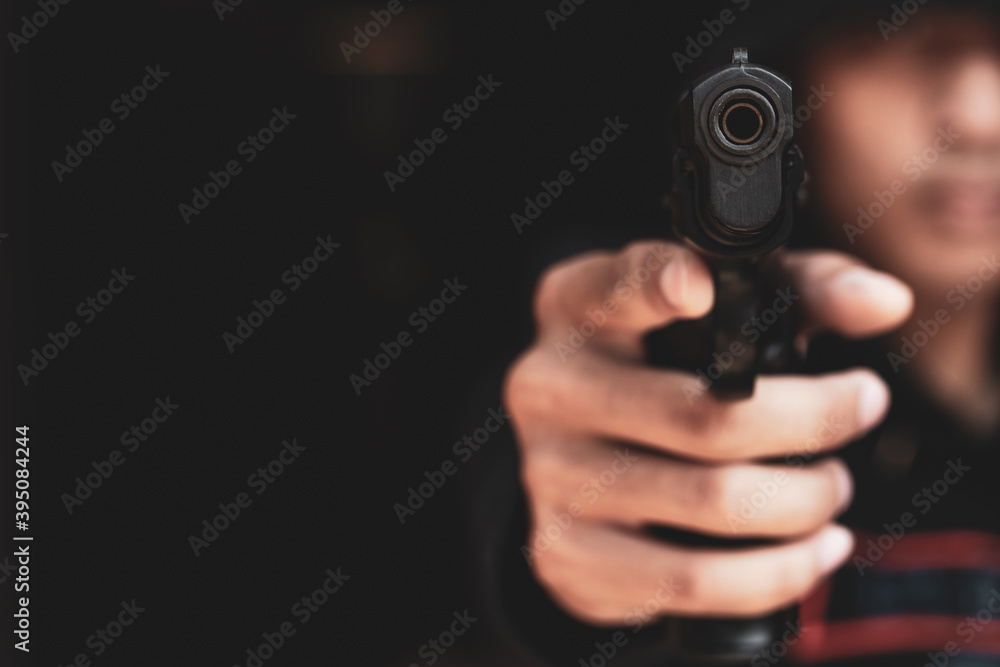 The gangster aimed a gun at the camera. A thief pointing a gun at the target on dark background. selective focus on front gun, Blurred focus. The gangster aimed a gun at the camera. A thief pointing a gun at the target on dark background. selective focus on front gun, Blurred focus.
