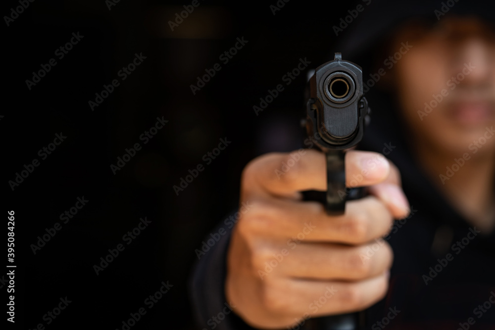 The gangster aimed a gun at the camera. A thief pointing a gun at the target on dark background. selective focus on front gun, Blurred focus.