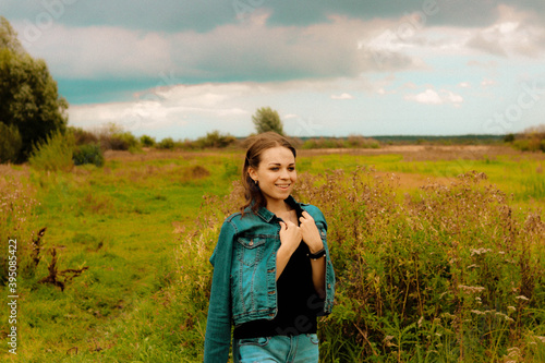 young girl in a denim jacket, jeans, standing in a field and smiling