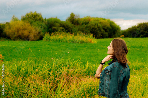 young girl in a denim jacket  jeans  standing in a field and smiling
