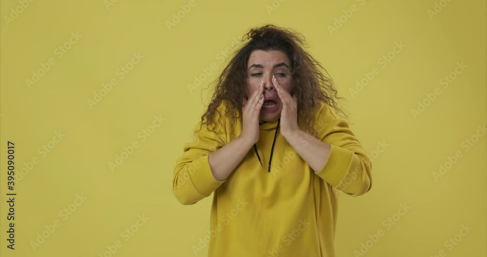 Sick woman covering mouth with hands while sneezing over yellow background Sick woman covering mouth with hands while sneezing over yellow background