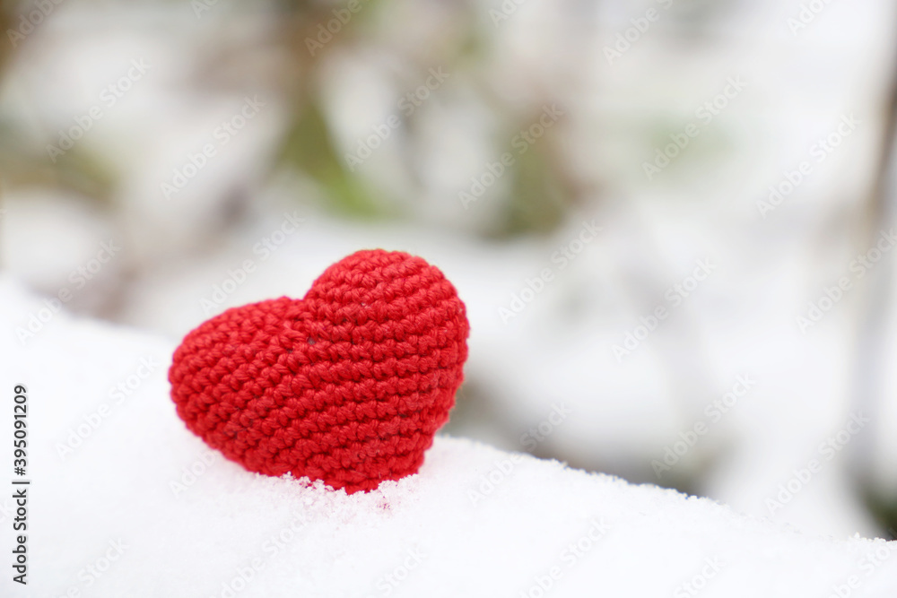 Fototapeta premium Love heart, red knitted symbol of passion in the snow in winter park. Background for Valentine's card