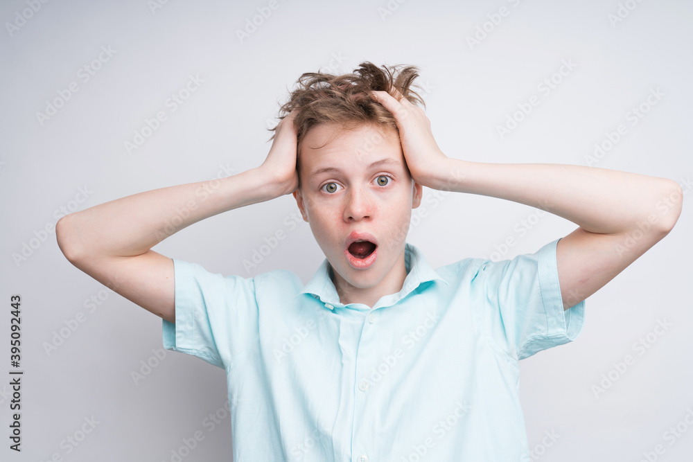 A mid shot of a caucasian boy on a white background. The boy is surprised about something, holding hands in his hair and ruffling it. His mouth is wide open and so his eyes A mid shot of a caucasian boy on a white background. The boy is surprised about something, holding hands in his hair and ruffling it. His mouth is wide open and so his eyes