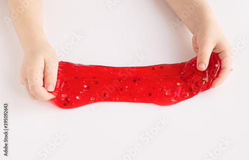 Child stretching colorful red slime to the sides. Kids hands playing slime toy on whate background. Making slime. Top view. Flatlay