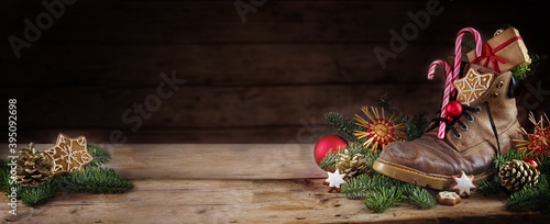 Old hiking boot filled with sweets, gifts and Christmas decoration, German tradition on Nicholas or Nikolaus day at 6th December, dark rustic wooden background with copy space, panoramic format