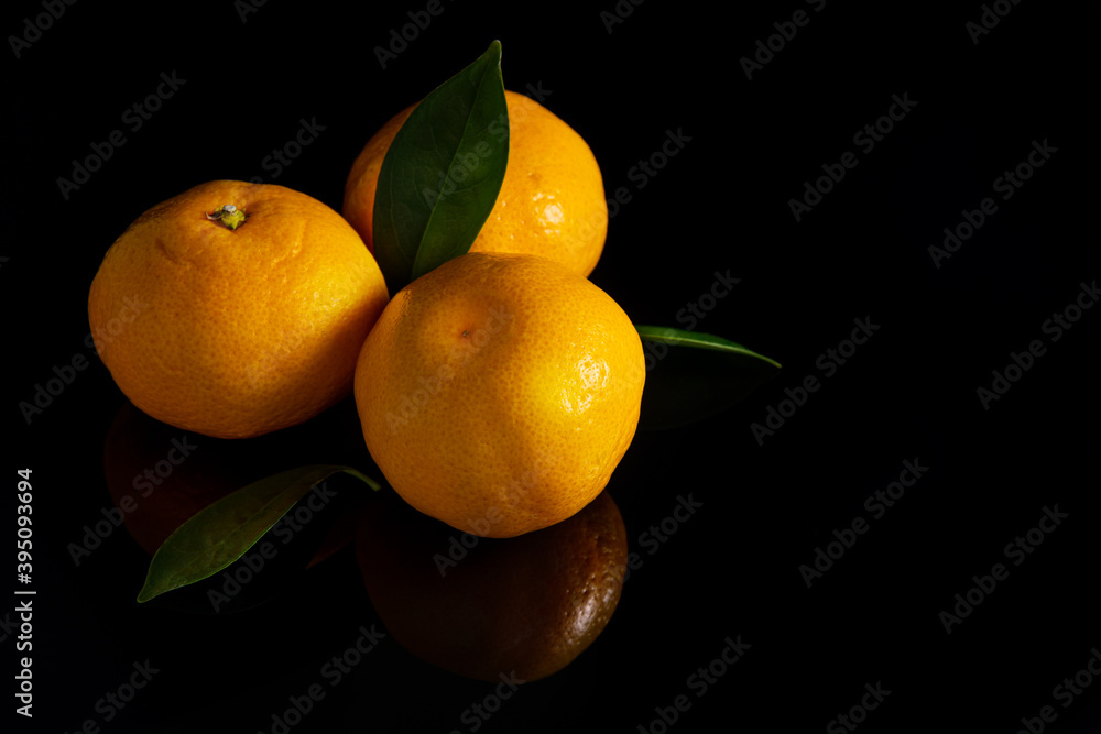 three ripe tangerines on a black background with a reflection