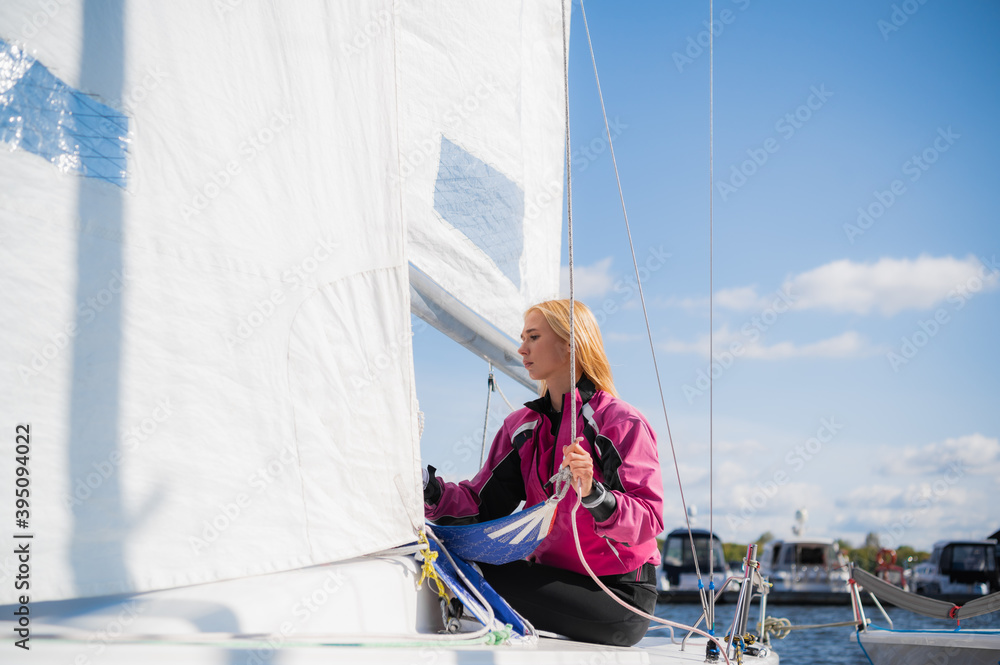 A young athlete in a pink jacket, conducts training on equipping a single-masted sports yacht on the river A young athlete in a pink jacket, conducts training on equipping a single-masted sports yacht on the river