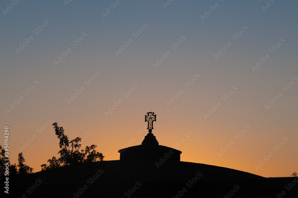 An openwork cross on the roof of an Orthodox monastery against the background of the evening sky
