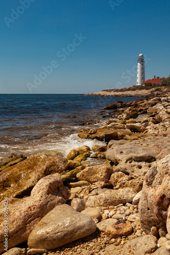 The white lighthouse stands on the seashore. In the foreground are picturesque stones