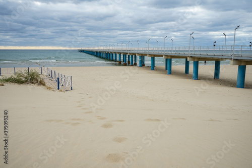 a long metal pier extends far out to sea and a beautiful view from the sand dunes