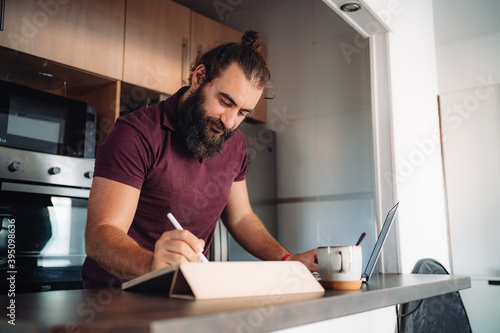 Bearded man working with computers from his kitchen bar at home