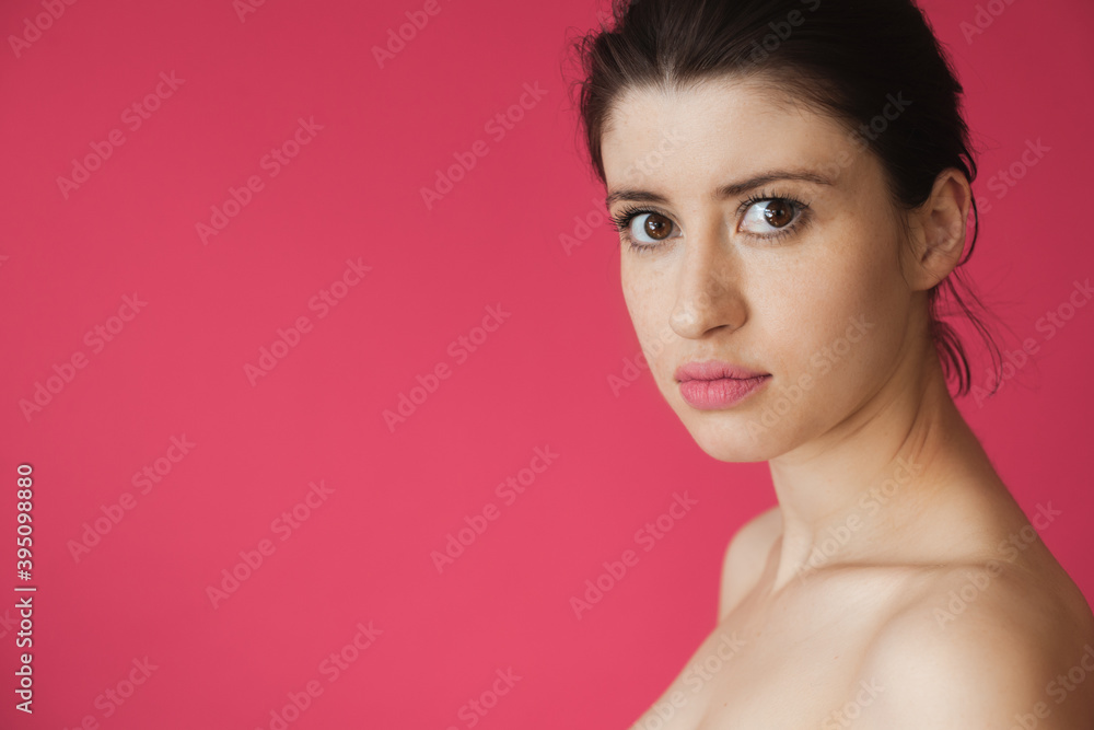 Caucasian woman with freckles and naked shoulders posing on a pink background with free space looking at camera Caucasian woman with freckles and naked shoulders posing on a pink background with free space looking at camera
