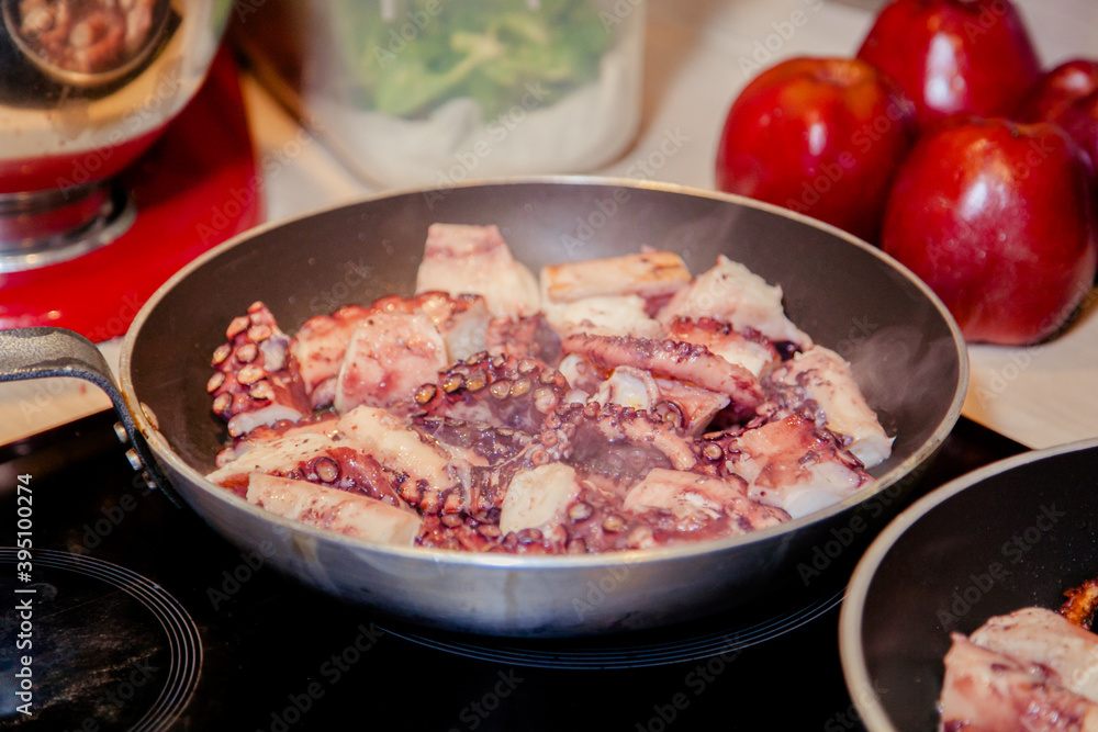 A pan full of grilled octopus in a kitchen with apples in the background A pan full of grilled octopus in a kitchen with apples in the background