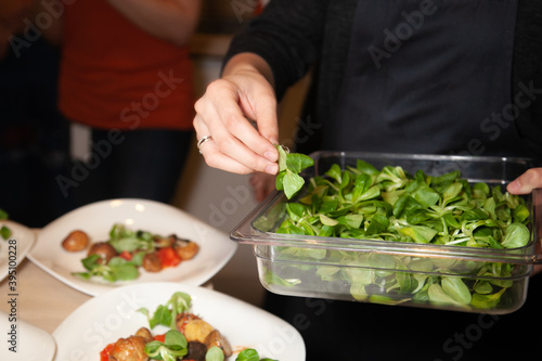 Woman holding a container full of fresh green leaves of spinach over a table with healthy decorated food