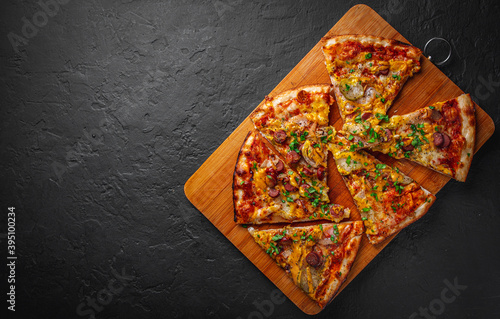 slice of Pizza with Mozzarella cheese, backon, ham, tomato sauce, pepper, sausage, pickled cucumbers and onion. Italian pizza on Dark grey black slate background
