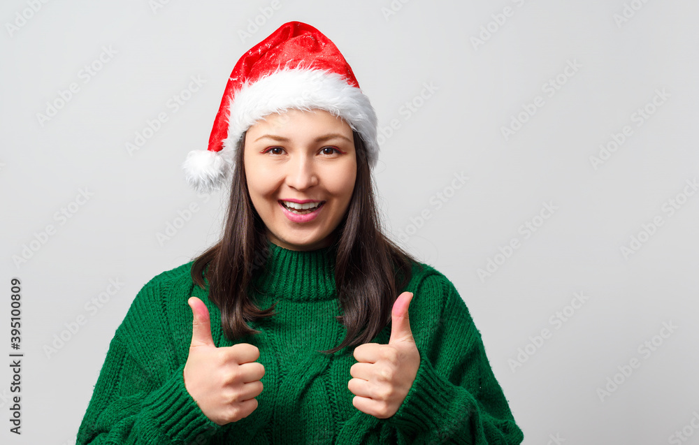 Young woman in Christmas hat showing thumb up gesture on a white background. Young woman in Christmas hat showing thumb up gesture on a white background.