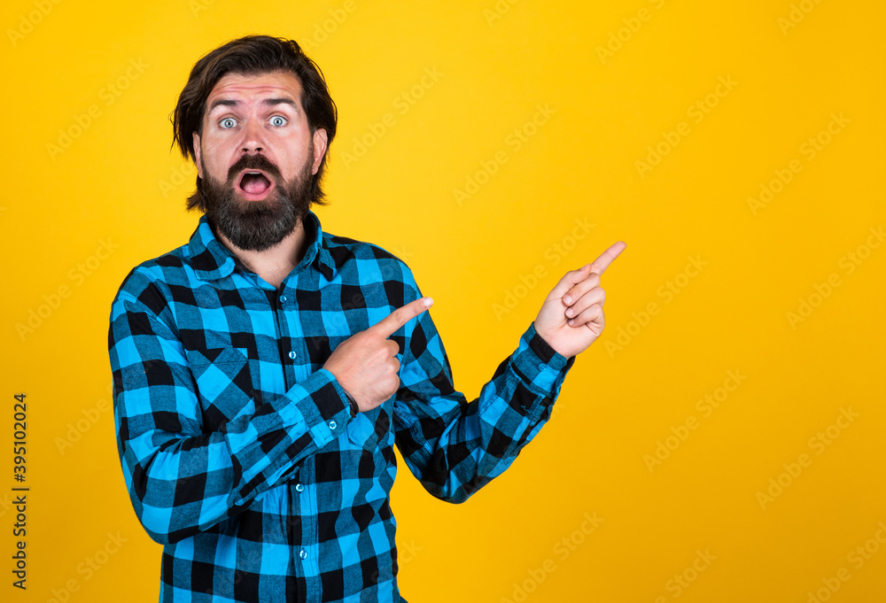surprised handsome hipster in checkered shirt pointing away while standing against yellow background, advertisement surprised handsome hipster in checkered shirt pointing away while standing against yellow background, advertisement