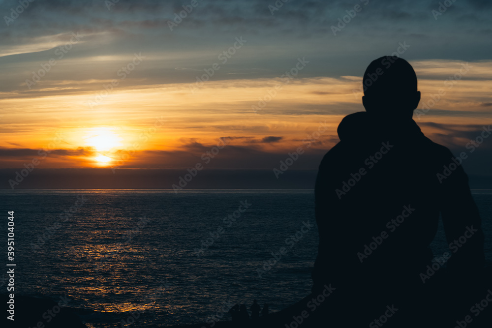 Portrait of the silhouette of a young man facing the sea at sunset. Relax concept