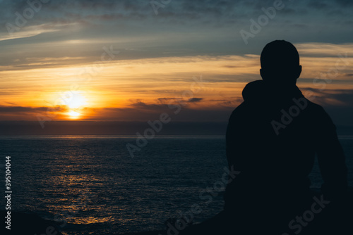 Portrait of the silhouette of a young man facing the sea at sunset. Relax concept
