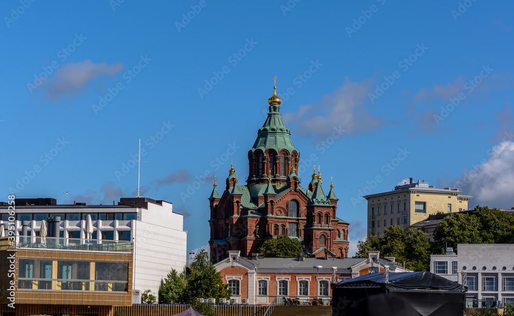 Red brick Uspenski Cathedral with green domes and golden crosses against blue sky. It is the main cathedral of the Orthodox Church of Finland.