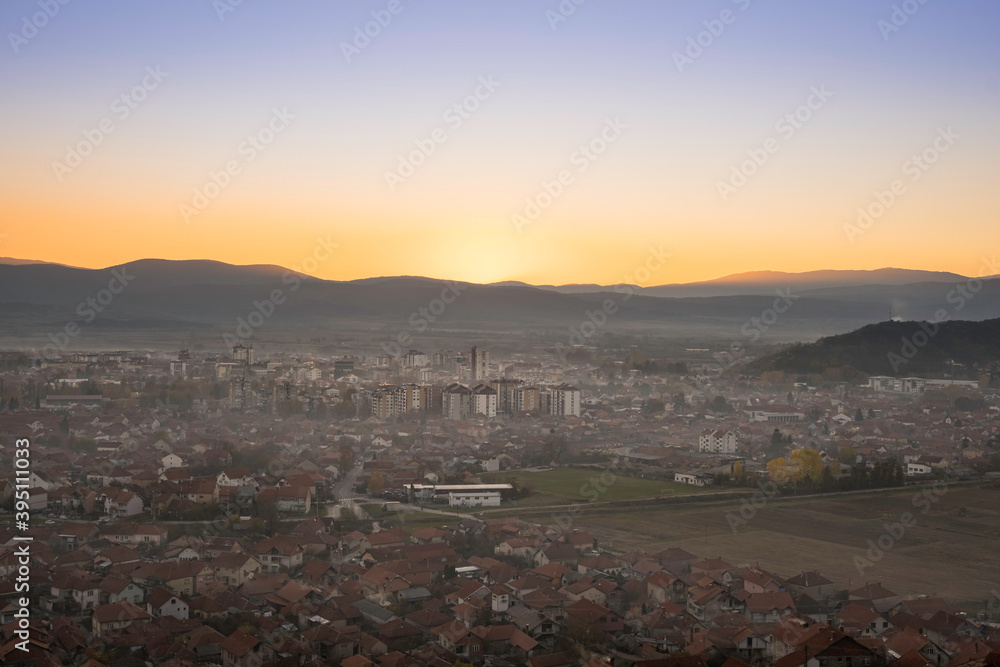 Beautiful, misy Pirot cityscape during golden hour, setting sun and distant horizon mountains