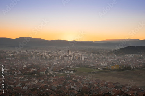 Beautiful, misy Pirot cityscape during golden hour, setting sun and distant horizon mountains