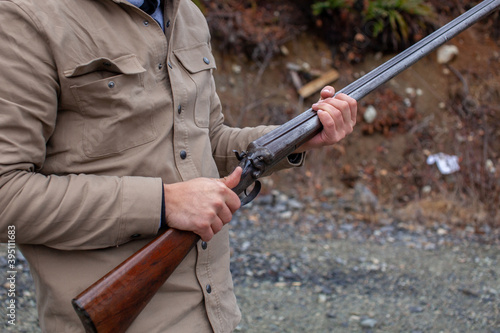 A man holds an old, antique, double-barrel shotgun to his waist, pointing the barrel downrange, ready to load. Outdoor range in Squamish, British-Columbia