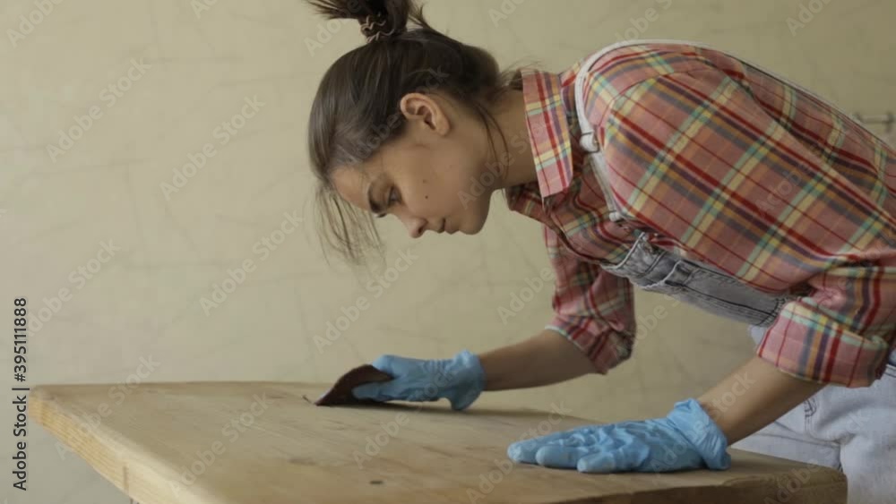 Busy artisan in protective gloves working in woodwork studio and polishing lumber table with rough sandpaper Busy artisan in protective gloves working in woodwork studio and polishing lumber table with rough sandpaper
