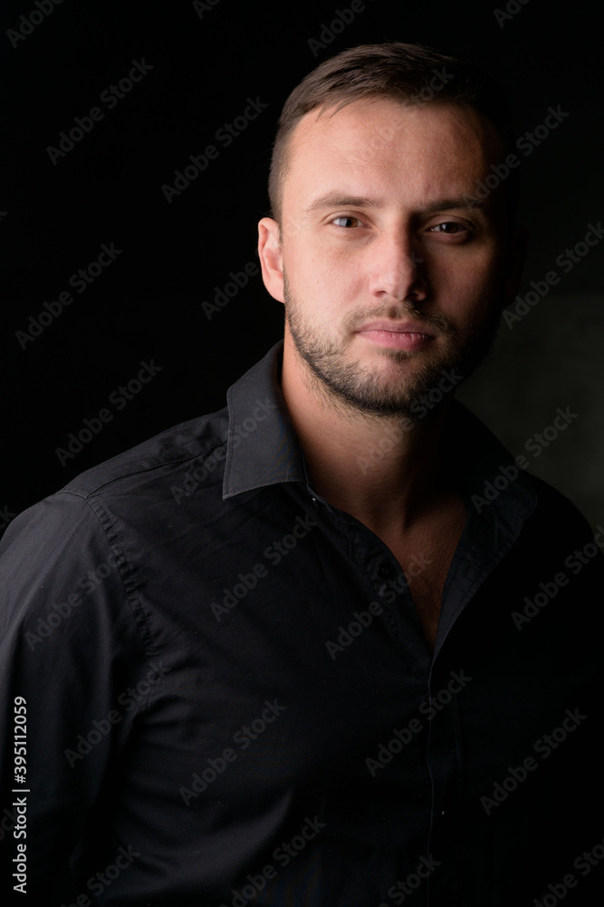 Studio portrait of a young caucasian man in a black blazer, looking at the camera, standing against plain studio background