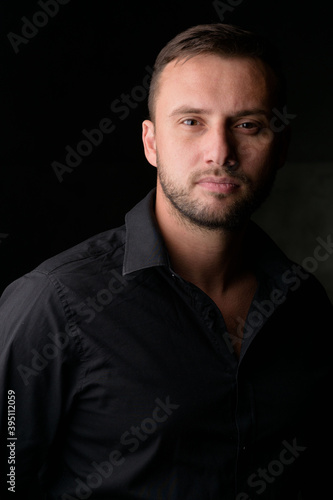 Studio portrait of a young caucasian man in a black blazer, looking at the camera, standing against plain studio background