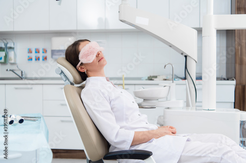 A female dentist wearing a formal medical suit relaxing in her office, while there are no patients.