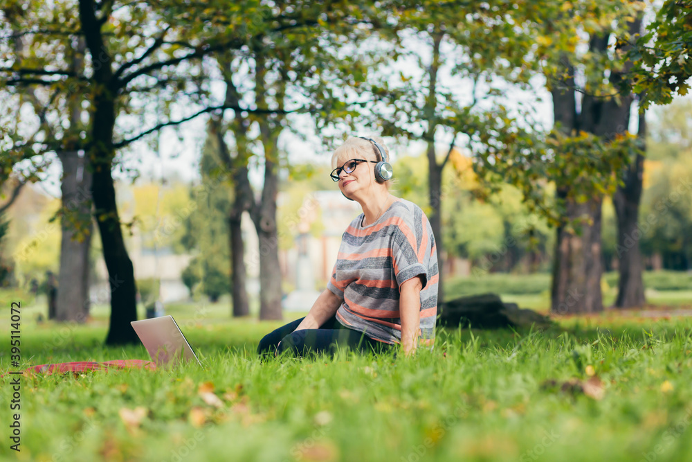 Senior woman resting in the park sitting on the grass, using phone and laptop, and reading a book Senior woman resting in the park sitting on the grass, using phone and laptop, and reading a book