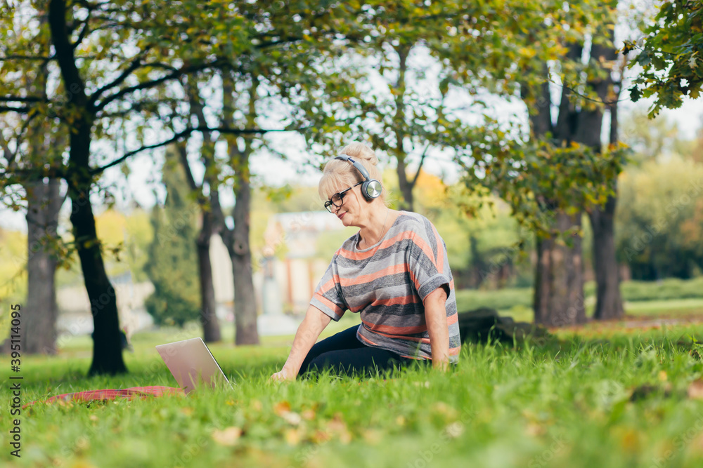 Senior woman resting in the park sitting on the grass, using phone and laptop, and reading a book Senior woman resting in the park sitting on the grass, using phone and laptop, and reading a book